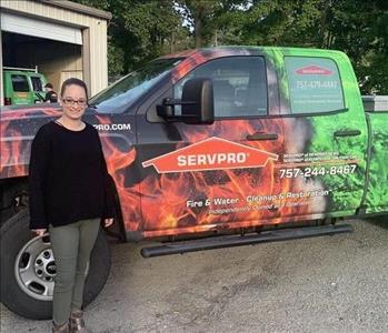 Female employee with light hair standing in front of SERVPRO vehicle