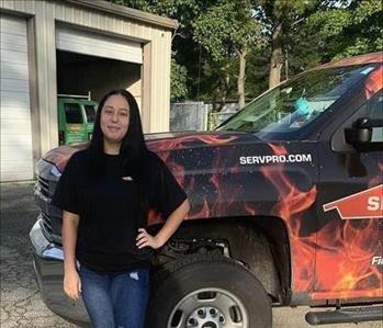 Female employee with dark hair standing in front of SERVPRO vehicle